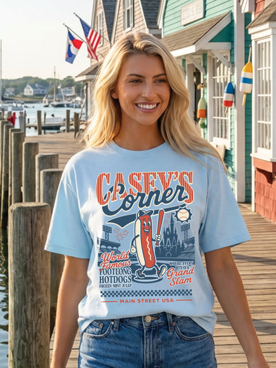Woman wearing a 'Casey's Corner' t-shirt on a dock with waterfront houses in the background